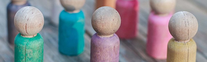 Bunte Holzspielfiguren in einer Gruppe auf einem rustikalen Holzuntergrund.